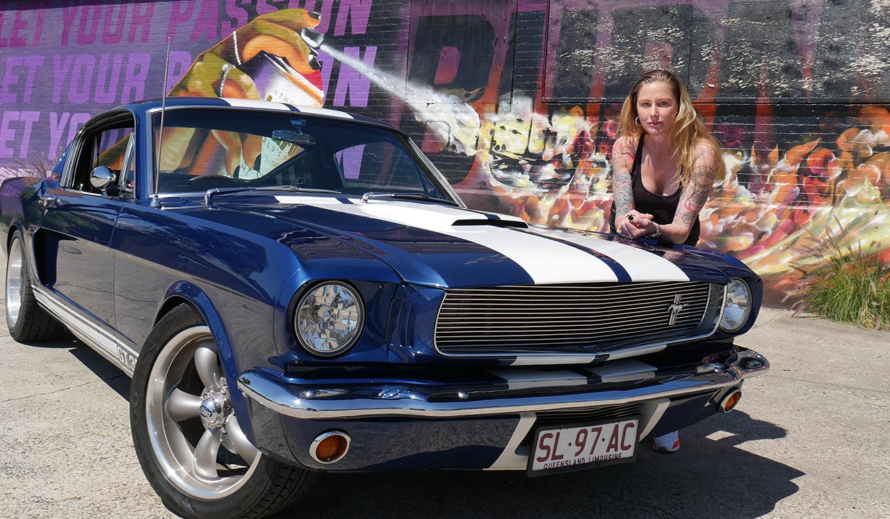 Blue Shelby 1965 Mustang Fastback driving off into the sunset and city scape view of Brisbane